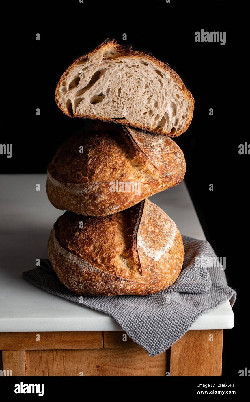 Leckeres Sauerteigbrot mit brauner Kruste auf Marmortisch vor schwarzem Hintergrund Stockfoto