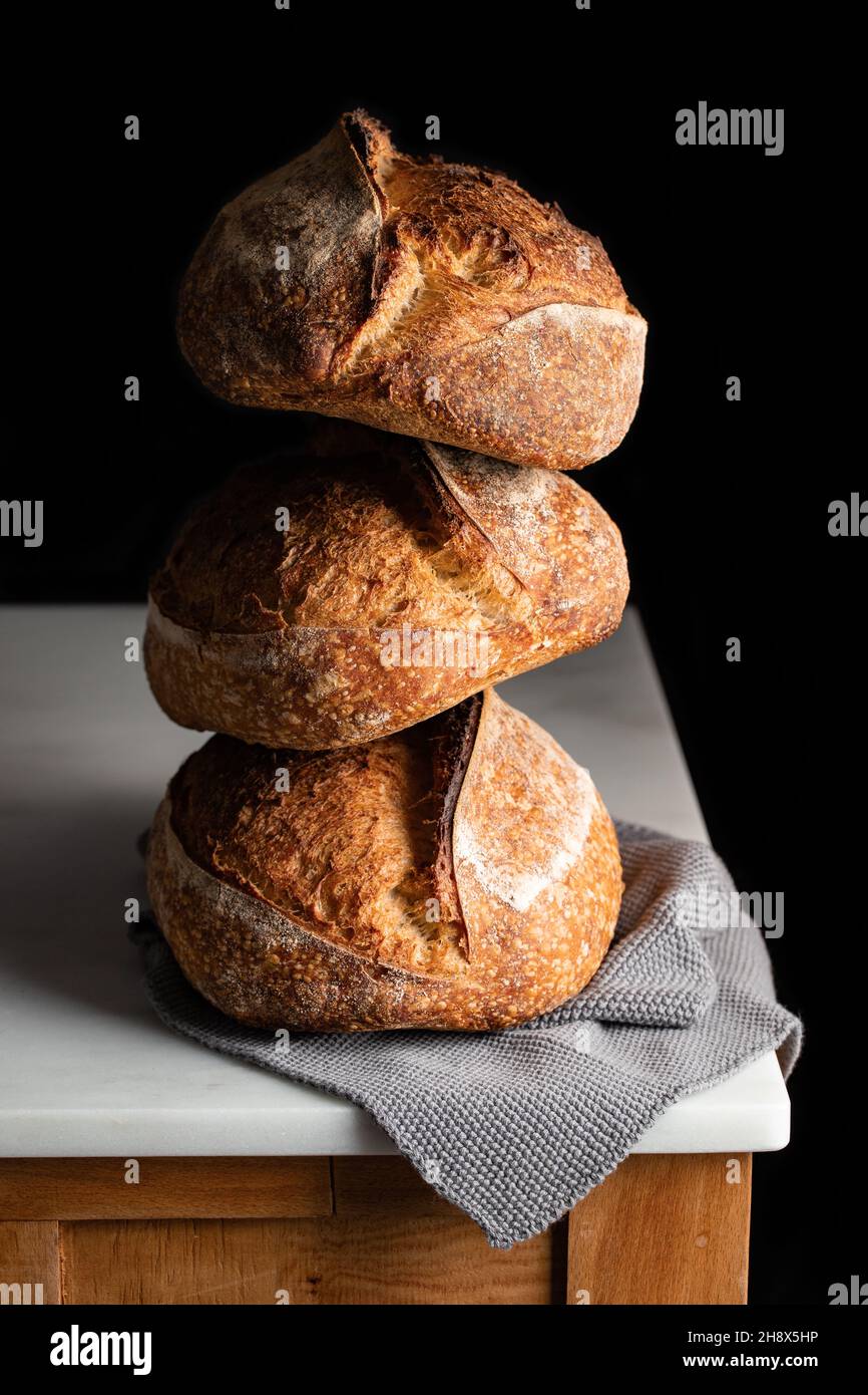 Leckeres Sauerteigbrot mit brauner Kruste auf Marmortisch vor schwarzem Hintergrund Stockfoto