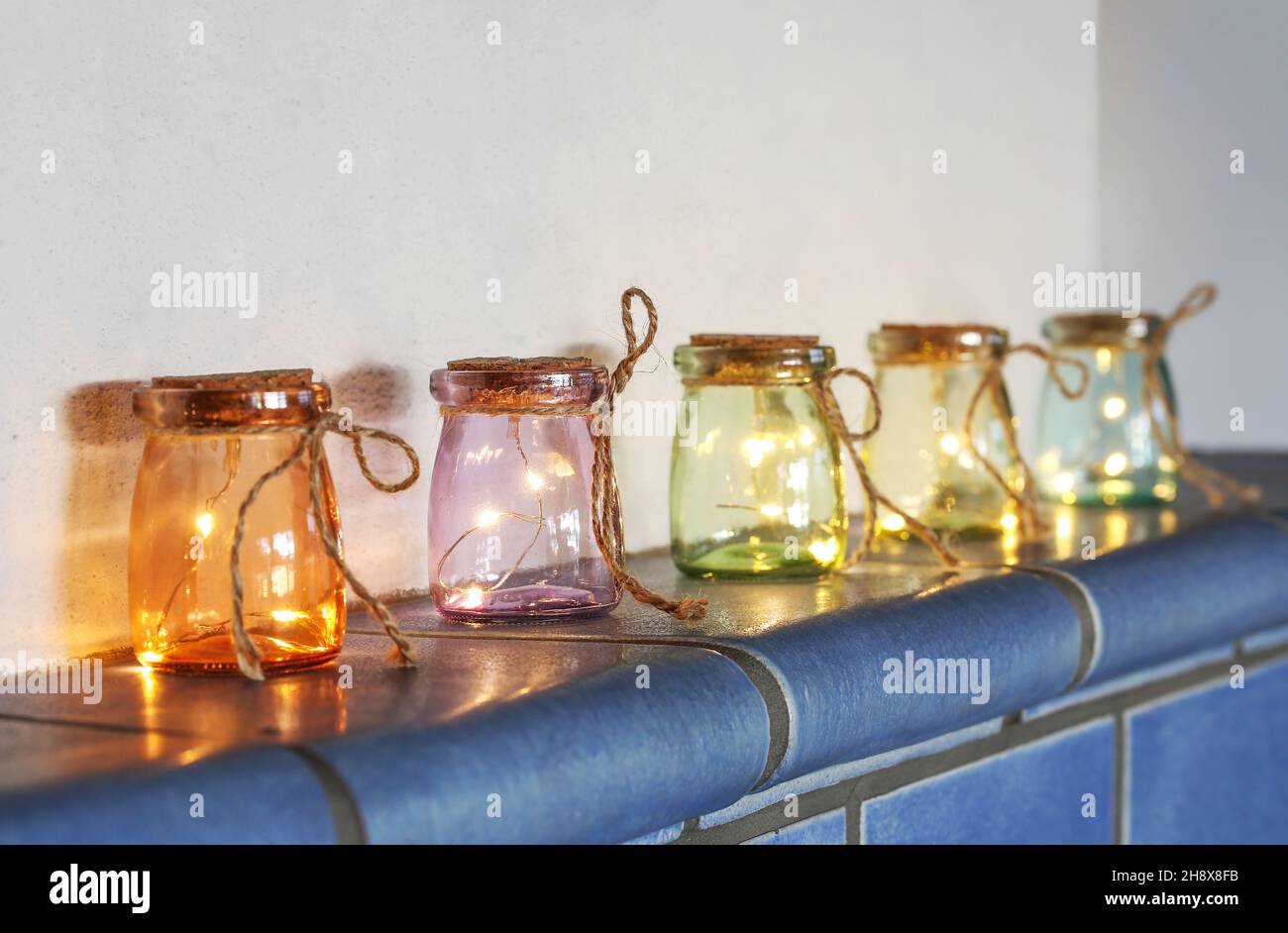 LED-Leuchten in farbigen Gläsern auf Kachelofen Stockfoto