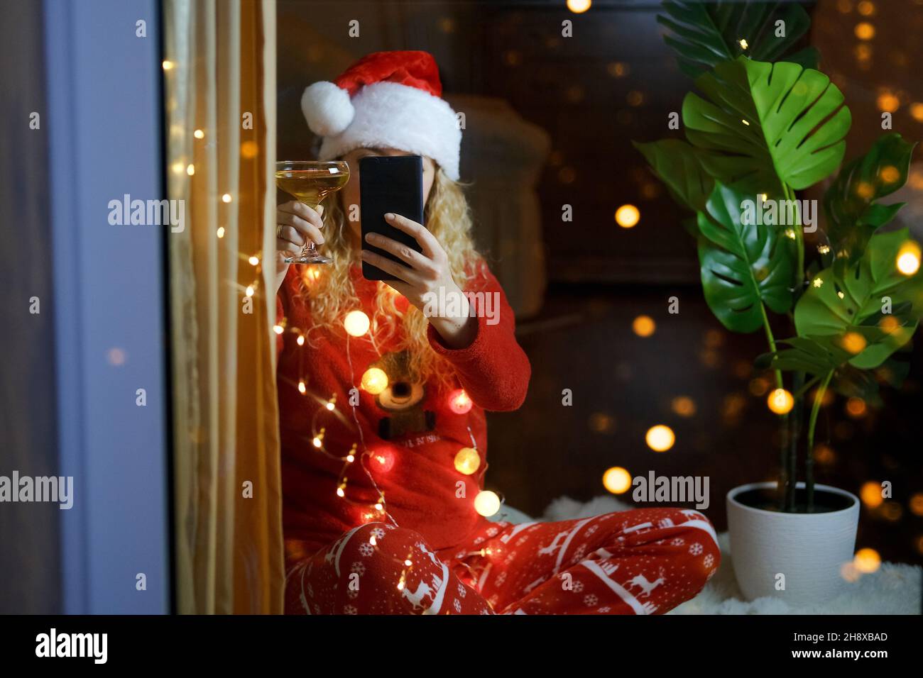 Frau in Weihnachtshut und Champagner feiert Silvester zu Hause mit Videoanruf Stockfoto