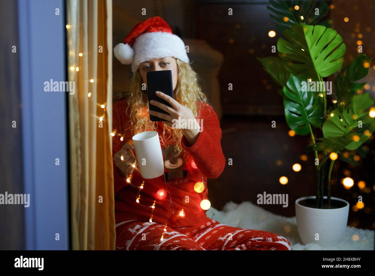 Frau in Weihnachtshut und Champagner feiert Silvester zu Hause mit Videoanruf Stockfoto