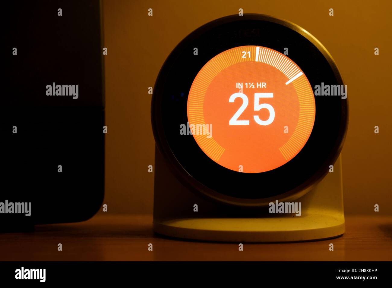 Ein intelligenter Lernthermostat für die Heimheizung von Nest befindet sich in einem Haus und wird so eingestellt, dass die Wärme von der aktuellen Umgebungstemperatur auf 25 Grad erhöht wird Stockfoto