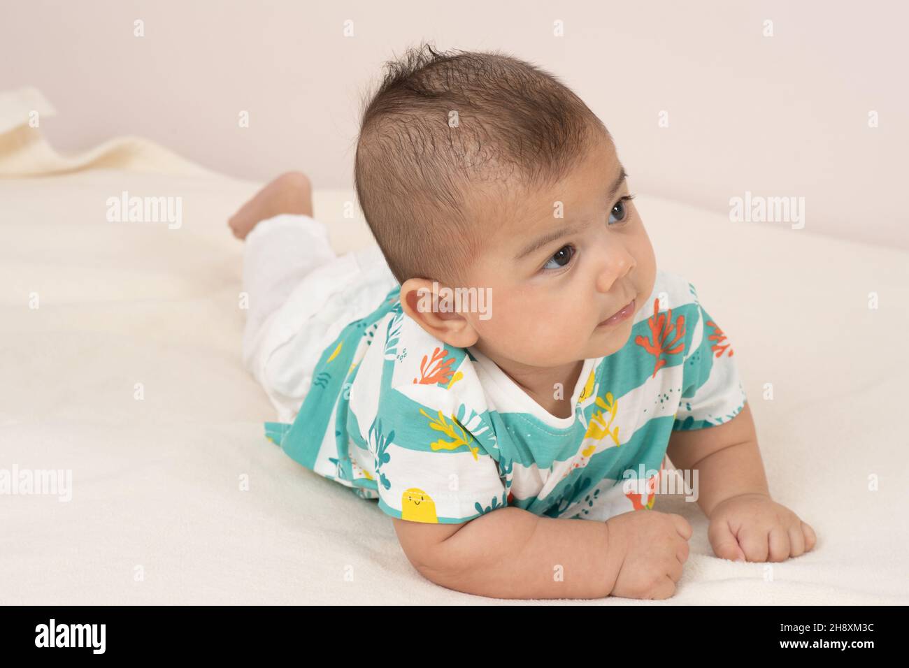 3 Monate alter Junge auf Bauch voller Länge hält Kopf nach oben und schaut zur Seite Stockfoto