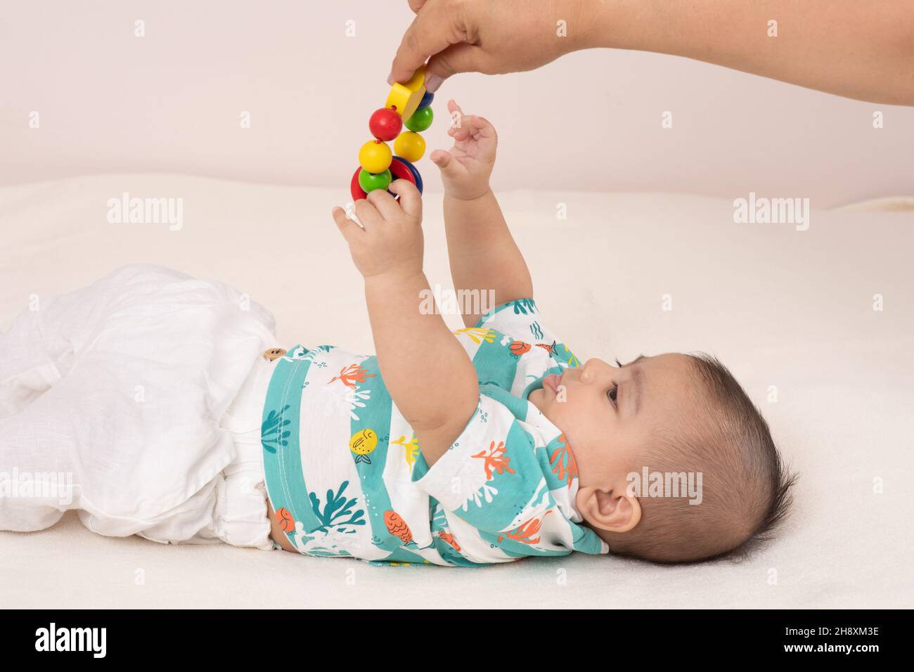 Der 3 Monate alte Junge auf dem Rücken, der nach einem Spielzeug-Erwachsenen greift, hält baumelnd über ihm Stockfoto