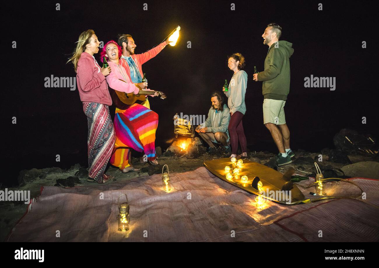 Junge Hipster-Freunde, die gemeinsam auf einer Strand-Campingparty mit Nachtfeuerlicht Spaß haben - Freundschaftsreisekonzept mit jungen Surfern Stockfoto