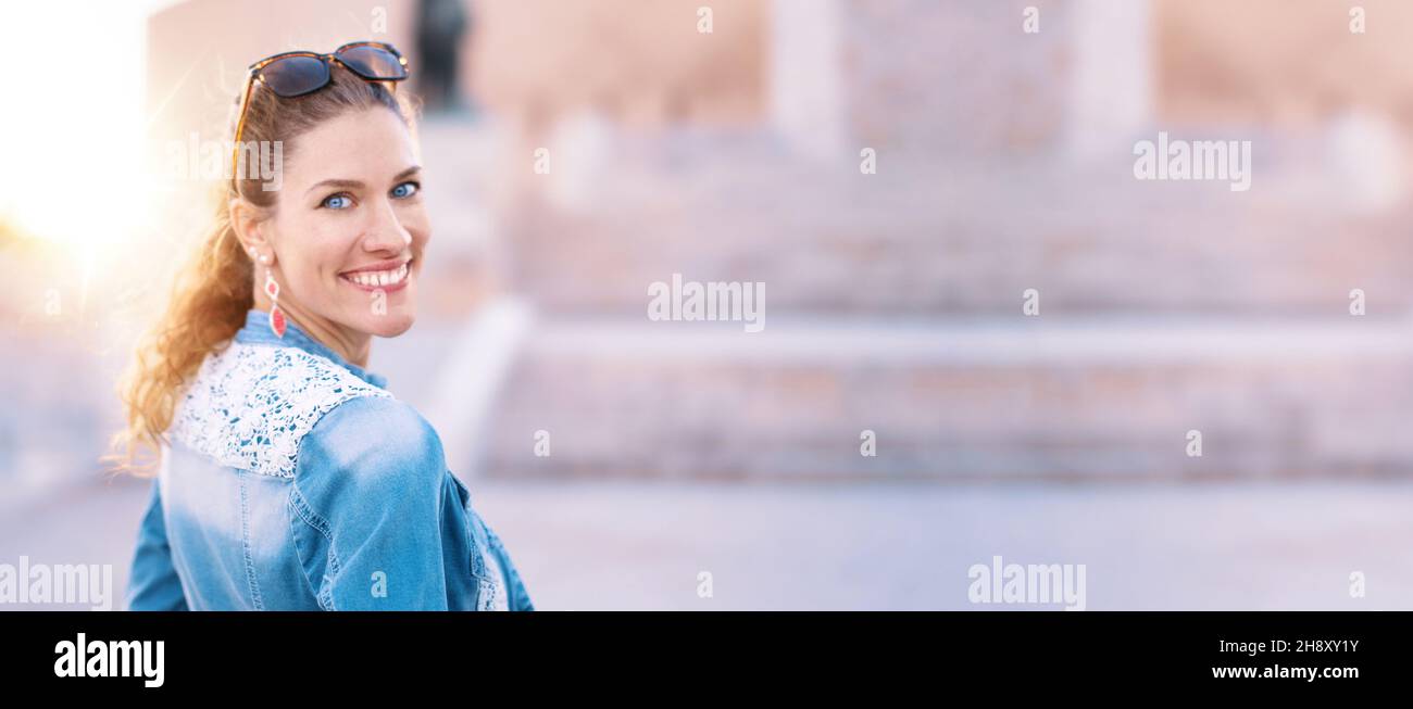 Junge kaukasische Frau in Denim-Jacke, die mit toothy Lächeln, Promotion-Breitbild-Banner zurückblickt Stockfoto