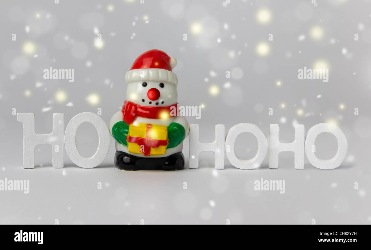 Weiße Buchstaben Ho-Ho-Ho und Schneemann Spielzeug auf weißem Hintergrund mit Bokeh Funken und Schneeflocken. Frohe Weihnachten und ein glückliches neues Jahr! Stockfoto