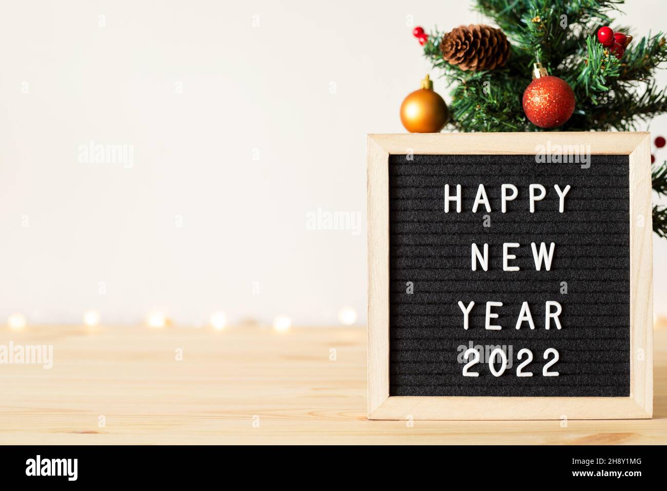 Frohes neues Jahr 2022 Grüße auf Briefbrett und Weihnachtsbaum mit Weihnachtsdekorationen auf Tisch Stockfoto