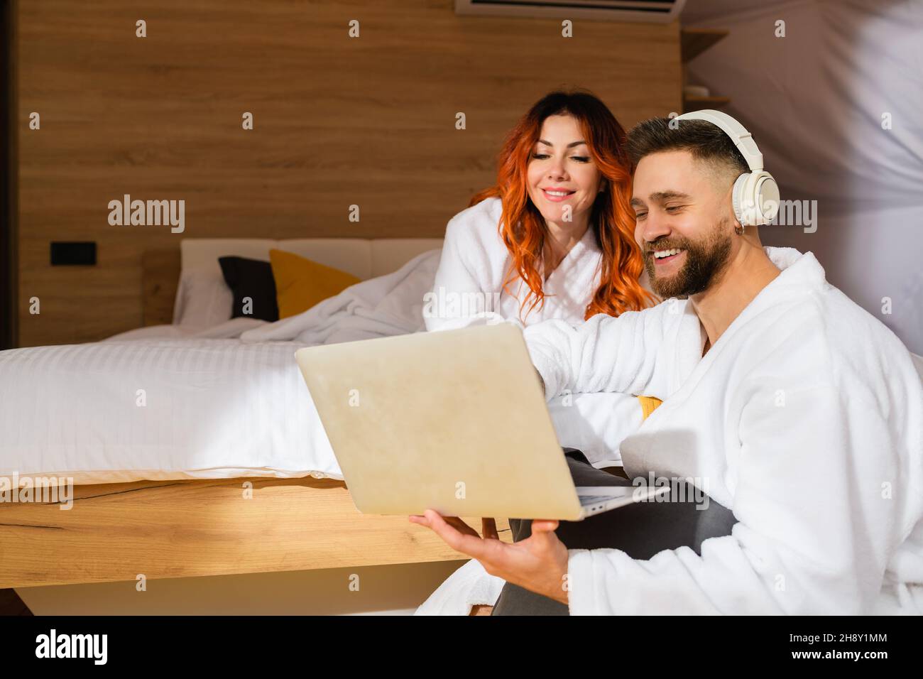 Junges Paar in Bademänteln, das mit einem Laptop auf dem Bett liegt. Mann und Frau schauen sich einen Film an. Blick von oben. Stockfoto
