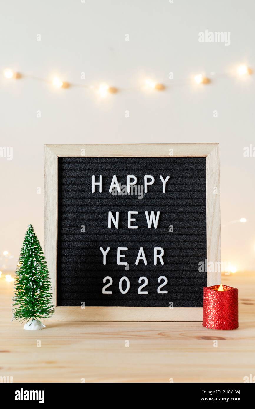 Frohes neues Jahr 2022 geschrieben auf schwarzem Filzbriefbrett und kleinem Weihnachtsbaum und Kerze auf Holztisch Stockfoto