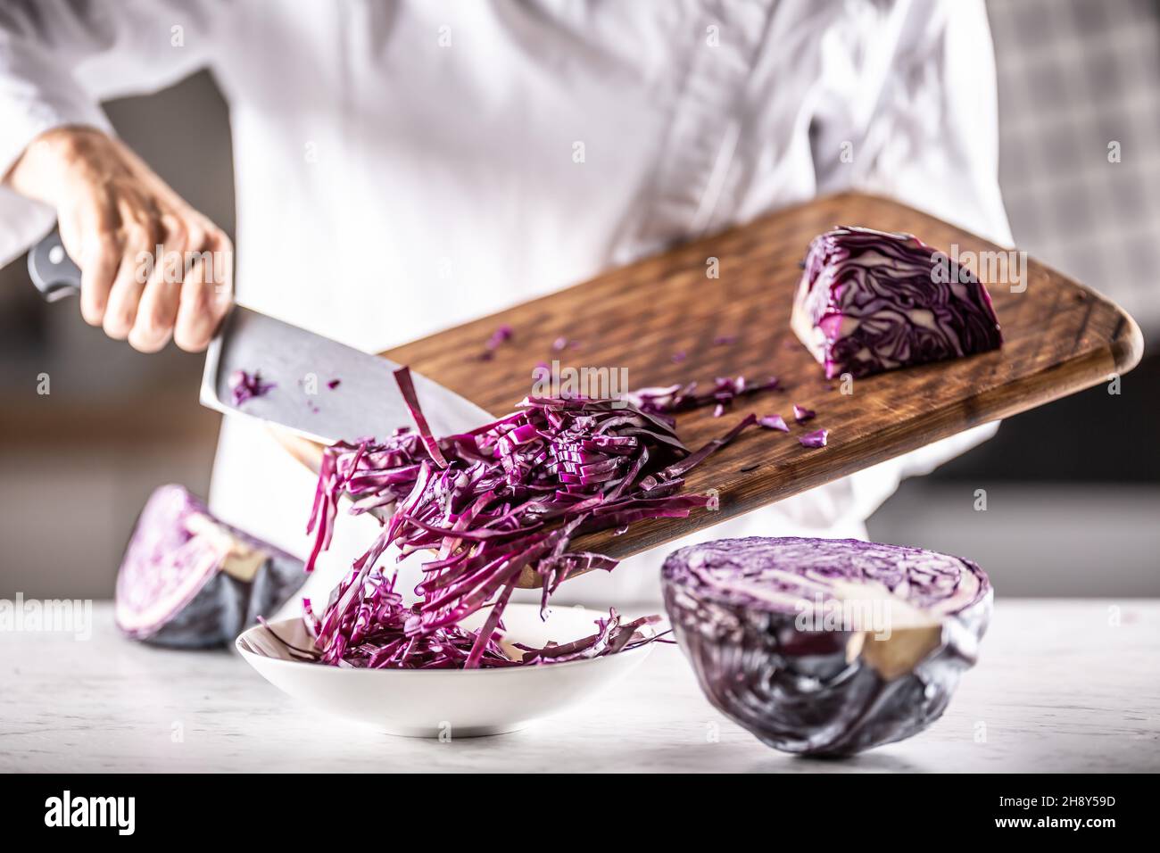 Rotkohl, zu kleinen Streifen zerkleinert, von einem Schneidebrett in eine Schüssel geben. Stockfoto