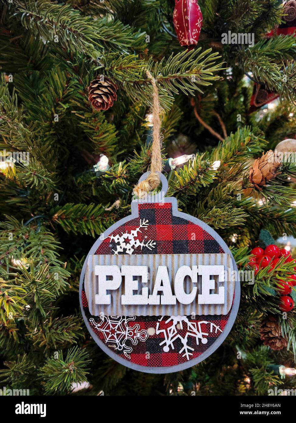 Nahaufnahme des Weihnachtsfriedens Ornaments auf einer Kiefer mit Weihnachtsbeleuchtung Stockfoto