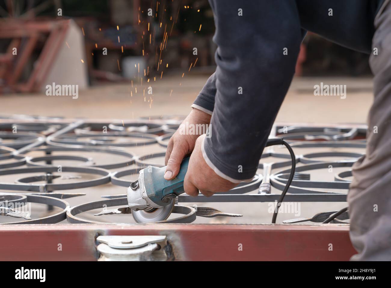 Mann grinst Metallzaun mit Winkelschleifer. Seitenansicht Stockfoto