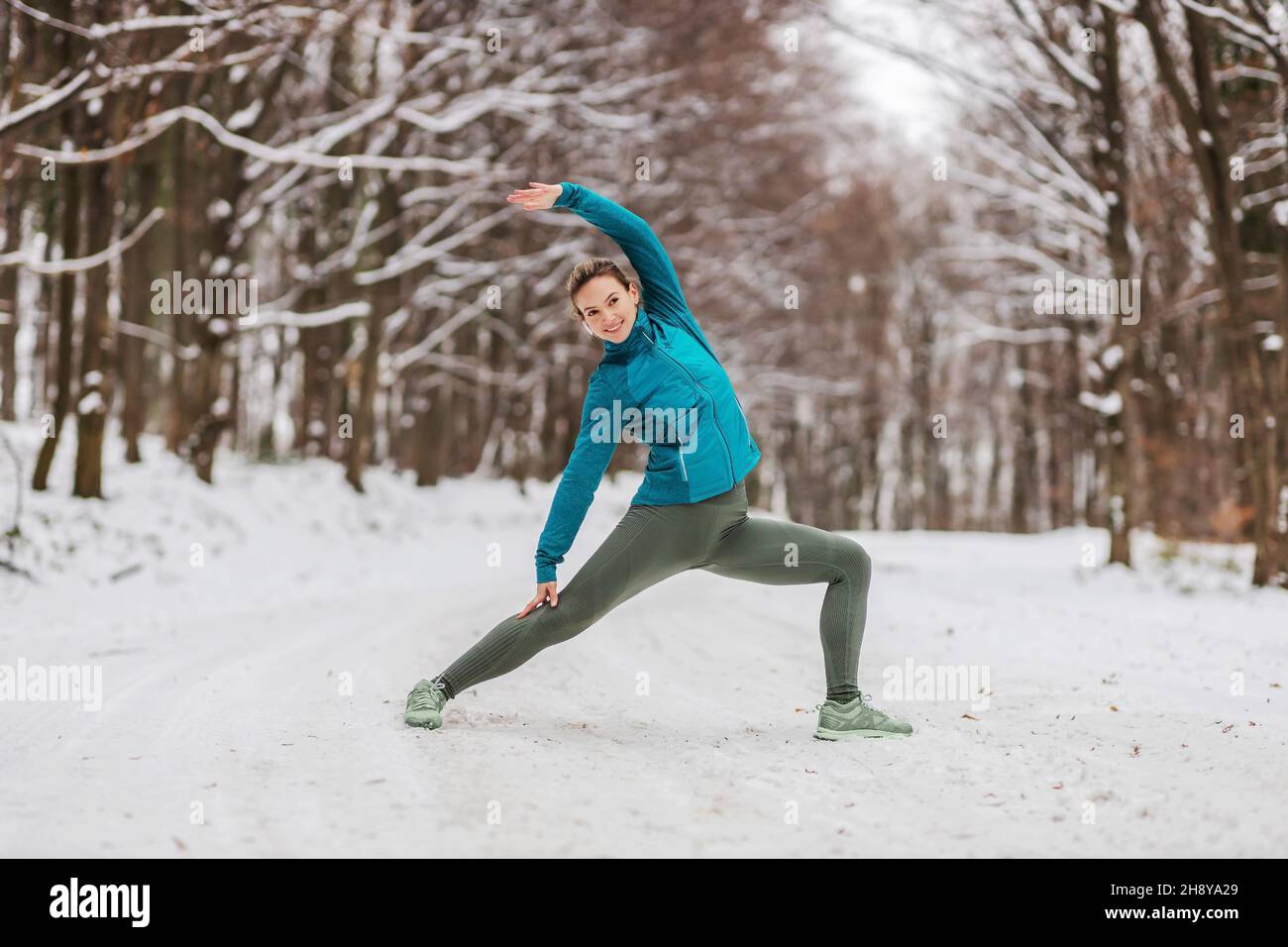 Sportlerin im warmen Outfit, die Yoga-Übungen im verschneiten Wald macht. Fitness im Freien, Schnee, Kälte, Winter Yoga Stockfoto