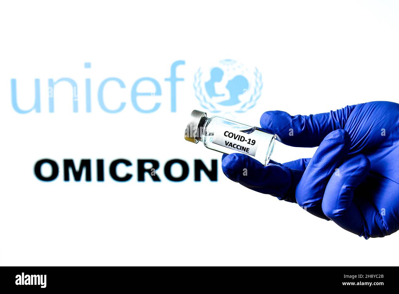 Madrid, Spanien – 29. November 2021: Handhaltefläschchen mit Covid-Impfstoff. UNICEF-Logo und Omicron covid Variant Word im Hintergrund geschrieben Stockfoto