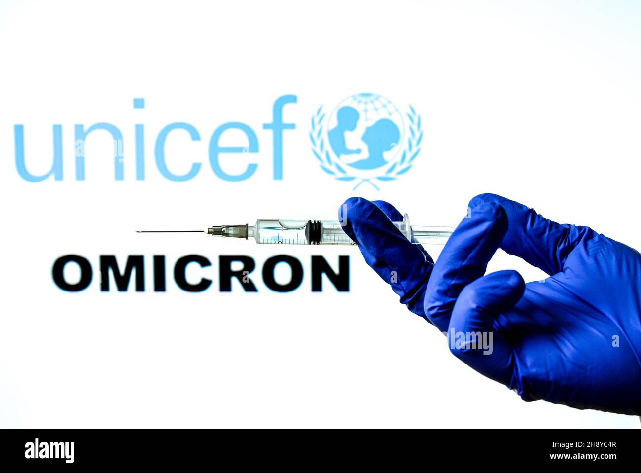 Madrid, Spanien - 29. November 2021: Handhaltende Spritze mit Covid-19-Impfstoff und UNICEF-Logo und neuem Omicron-Wort auf weißem Hintergrund. Stockfoto