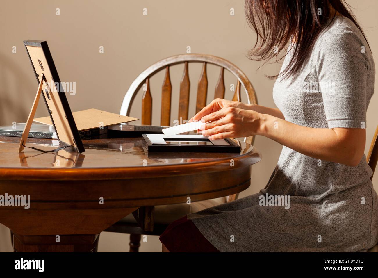 Eine junge kaukasische Frau platziert ein gedrucktes Foto in einen Bilderrahmen mit Ständer. Auf dem Tisch befinden sich weitere Rahmen. Tischbild Fra Stockfoto