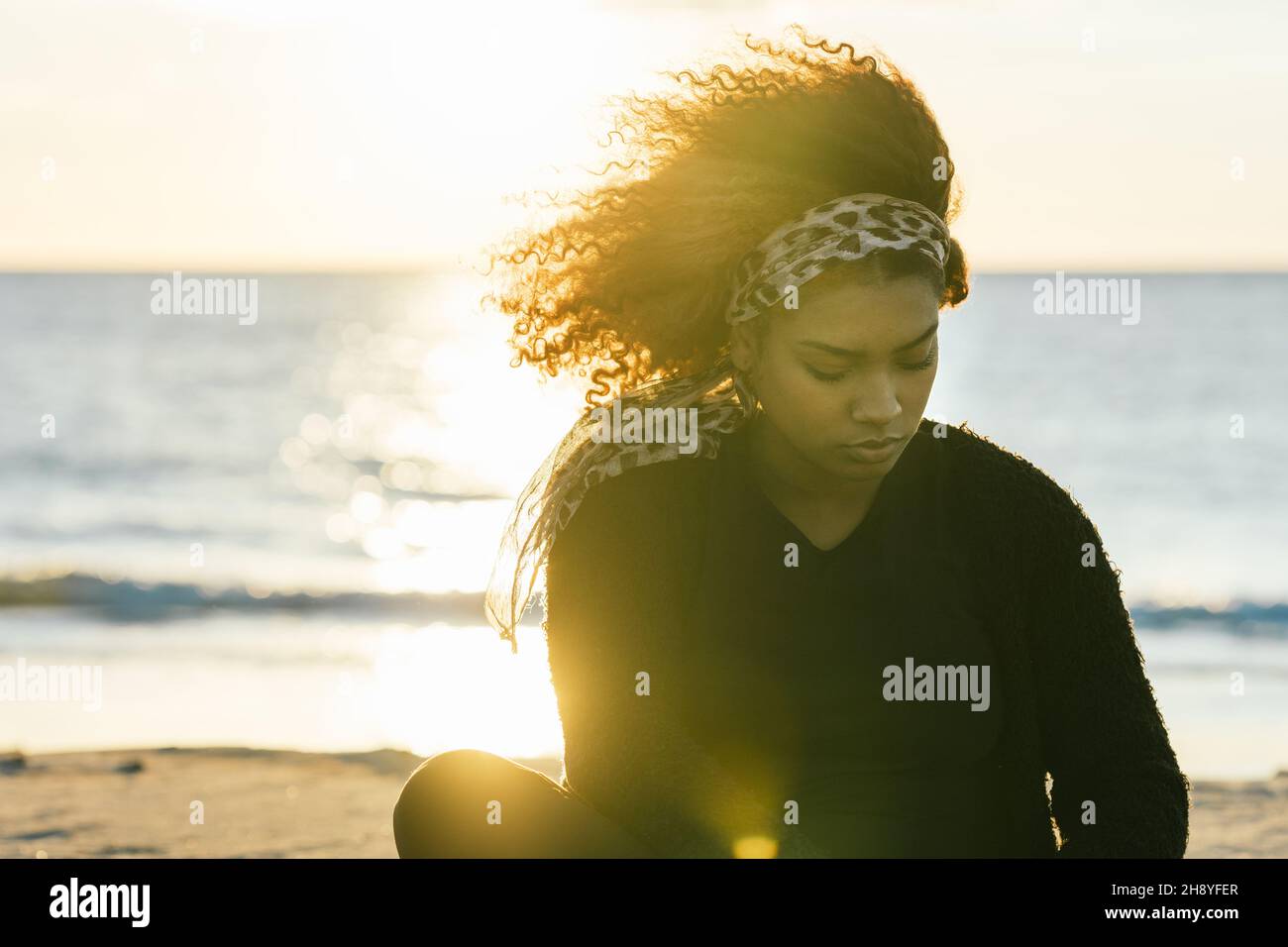Sonnenlicht beleuchtet eine Schwangerin, die nach einer Yoga-Sitzung am Strand sitzt Stockfoto