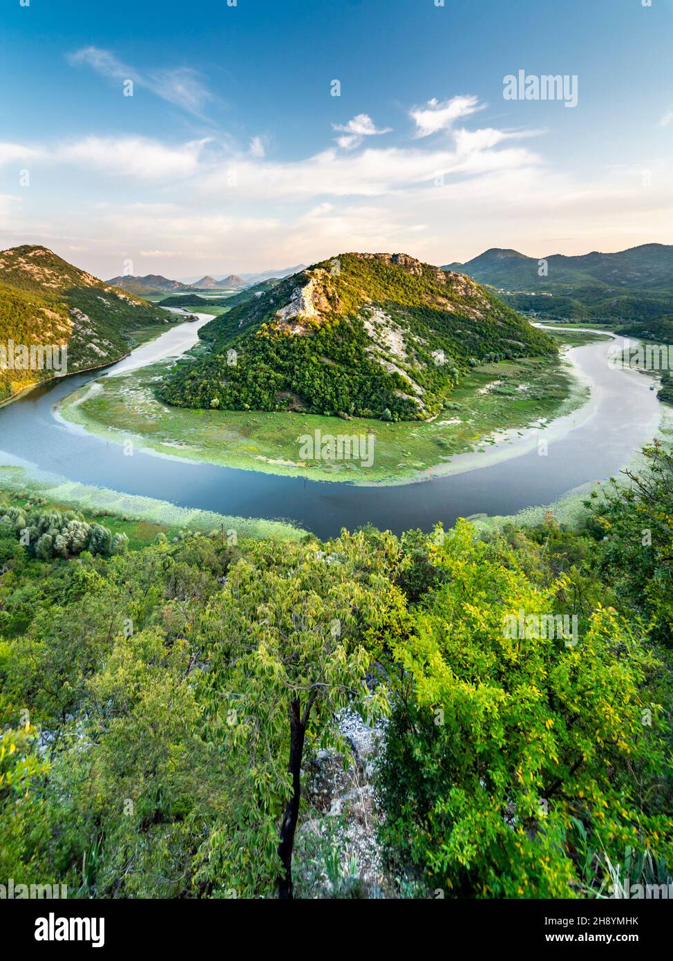 Blick vom Aussichtspunkt Pavlova Strana auf ein kleines Boot, das die Hufeisenkurve umrundet, und die albanischen Berge in der Ferne. Stockfoto