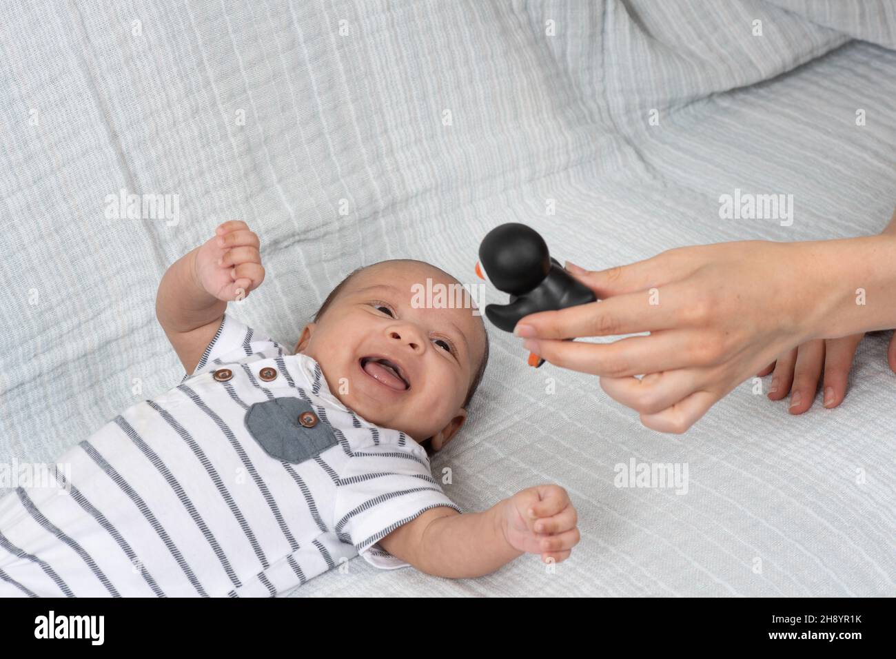 2 Monate altes Baby (früh) Nahaufnahme auf dem Rücken lacht als Reaktion auf schwarz-weißes Pinguin-Spielzeug mit hohem Kontrast Stockfoto