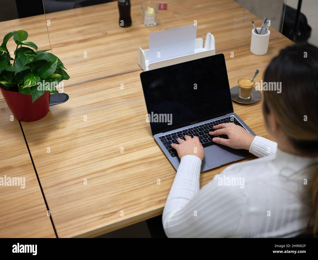 Blick von hinten auf eine Frau, die ihren Laptop in einem Coworking Space benutzt Stockfoto