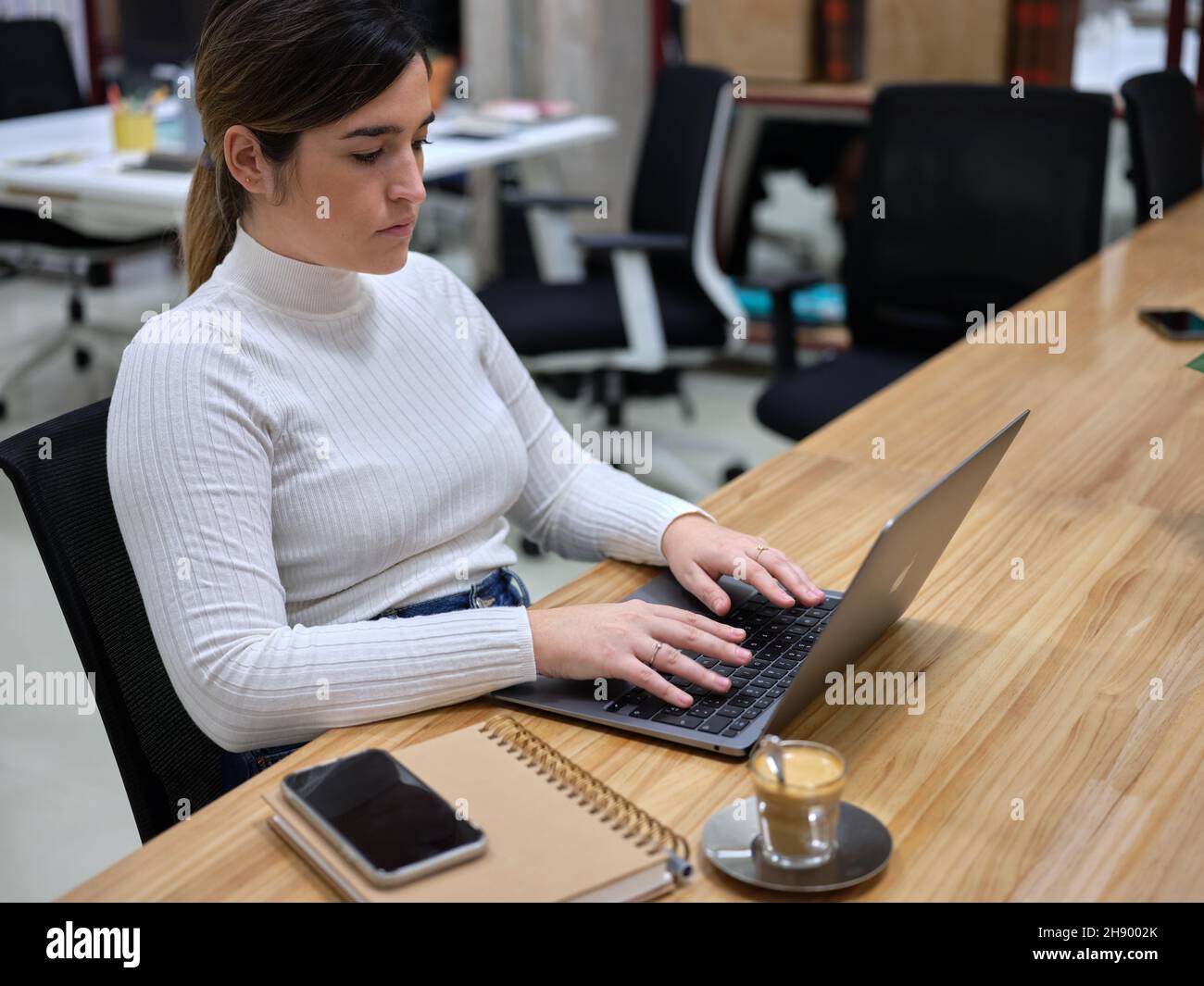 Frau in einem Arbeitsbereich, die ihren Computer mit einem Kaffee daneben benutzt Stockfoto