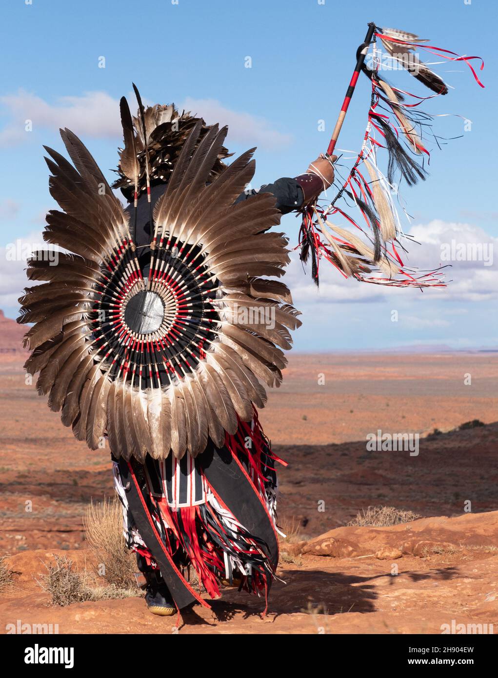 Nahaufnahme einer indigenen Person Amerikas, die von hinten fotografiert wurde, mit gefiedertem Kopfschmuck und Hektik und mit einem Stock mit Bändern. Stockfoto