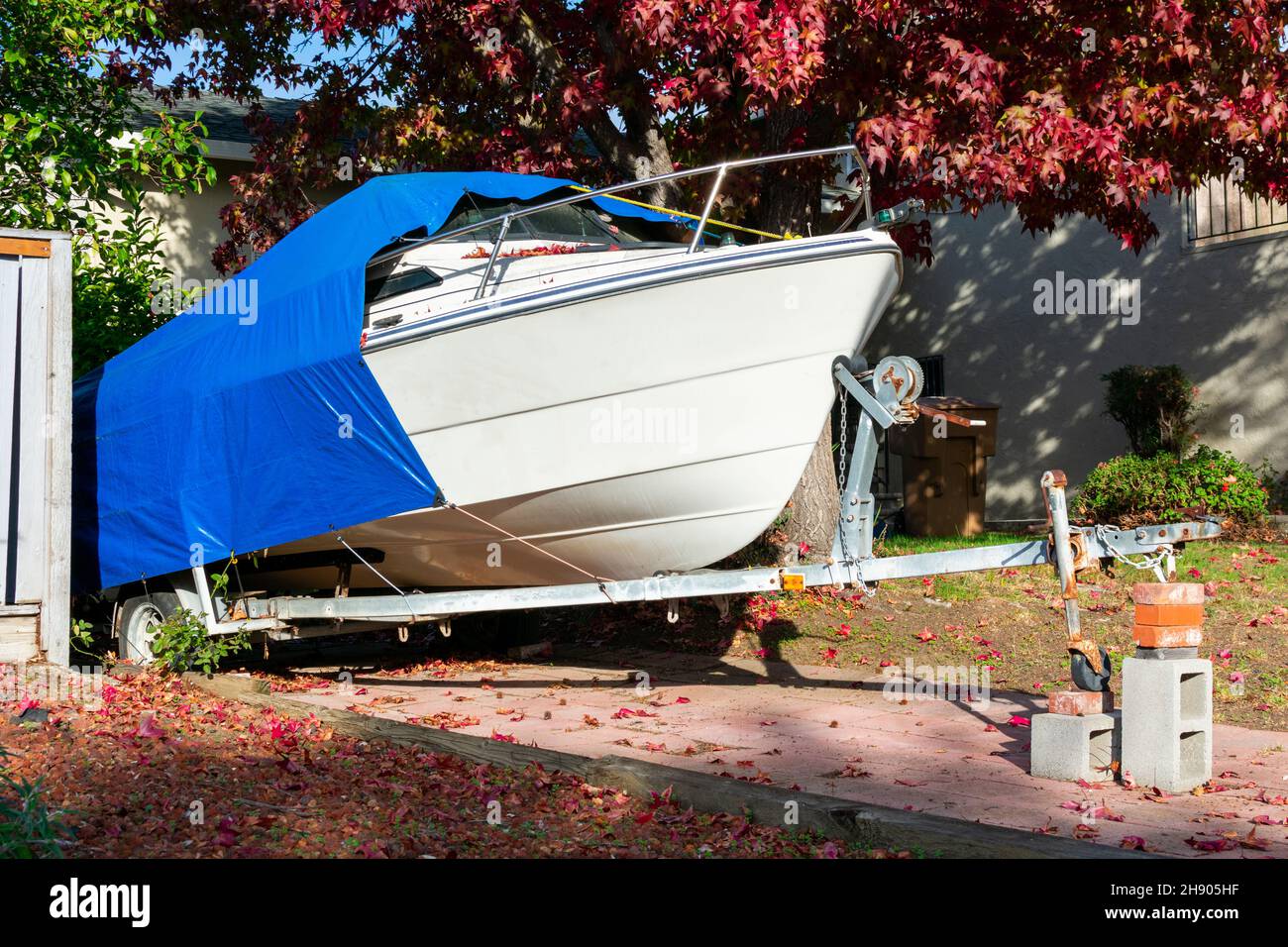 Freizeitboot auf Anhänger auf der Auffahrt des Wohnhauses gespeichert. Der Kreuzer ist zum Schutz mit einem blauen Tarp-Zelt überzogen. Stockfoto