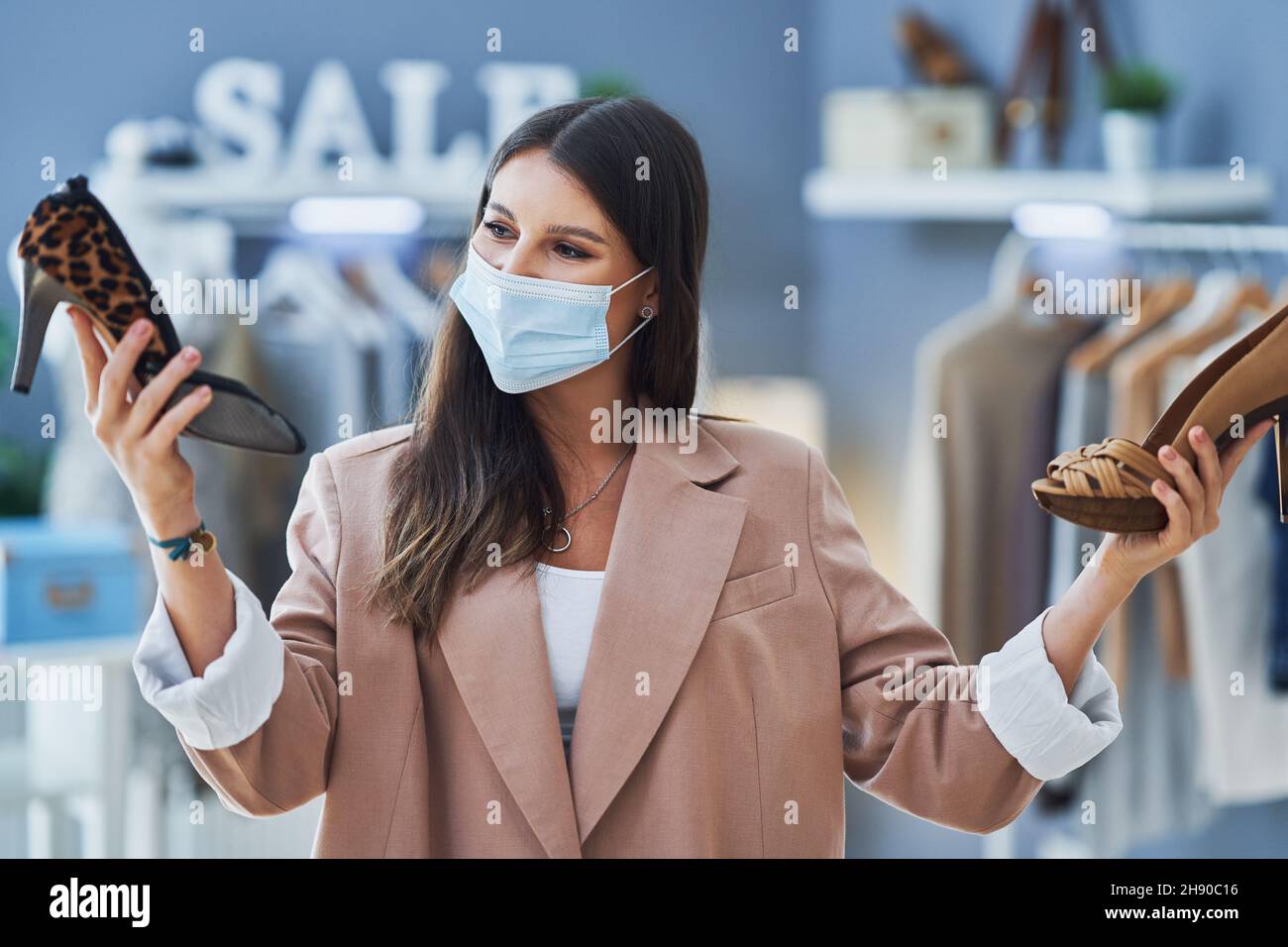 Junge nette Mädchen im Geschäft während des Einkaufens halten Schuhe tragen Maske Stockfoto
