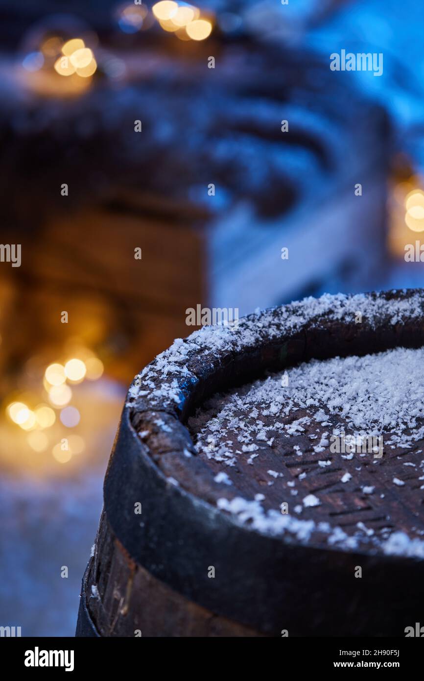 Hoher Winkel von Holzfass mit Schnee bedeckt im Wintergarten mit glühenden Girlande in der Nacht platziert Stockfoto