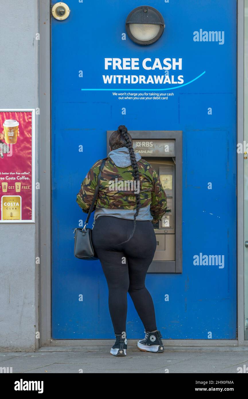 Junge BAME oder schwarze Frau mit Geldautomat, Frau mit Geldautomat, übergewichtige Frau mit Geldautomat, kostenloses Bargeld Widrawals, Übergewicht Gewichtszunahme. Stockfoto