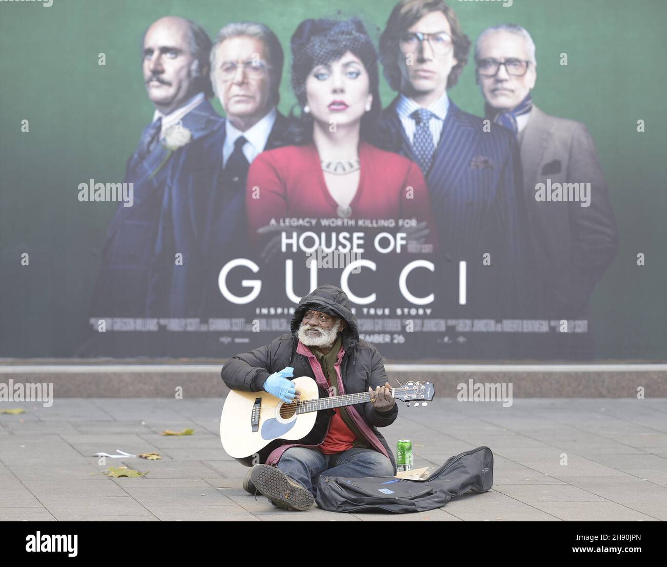 London, England, Großbritannien. Älterer schwarzer Mann, der auf dem Leicester Square vor einem Filmplakat für das Haus Gucci - Dezember 2021, anschellt/bettelt Stockfoto