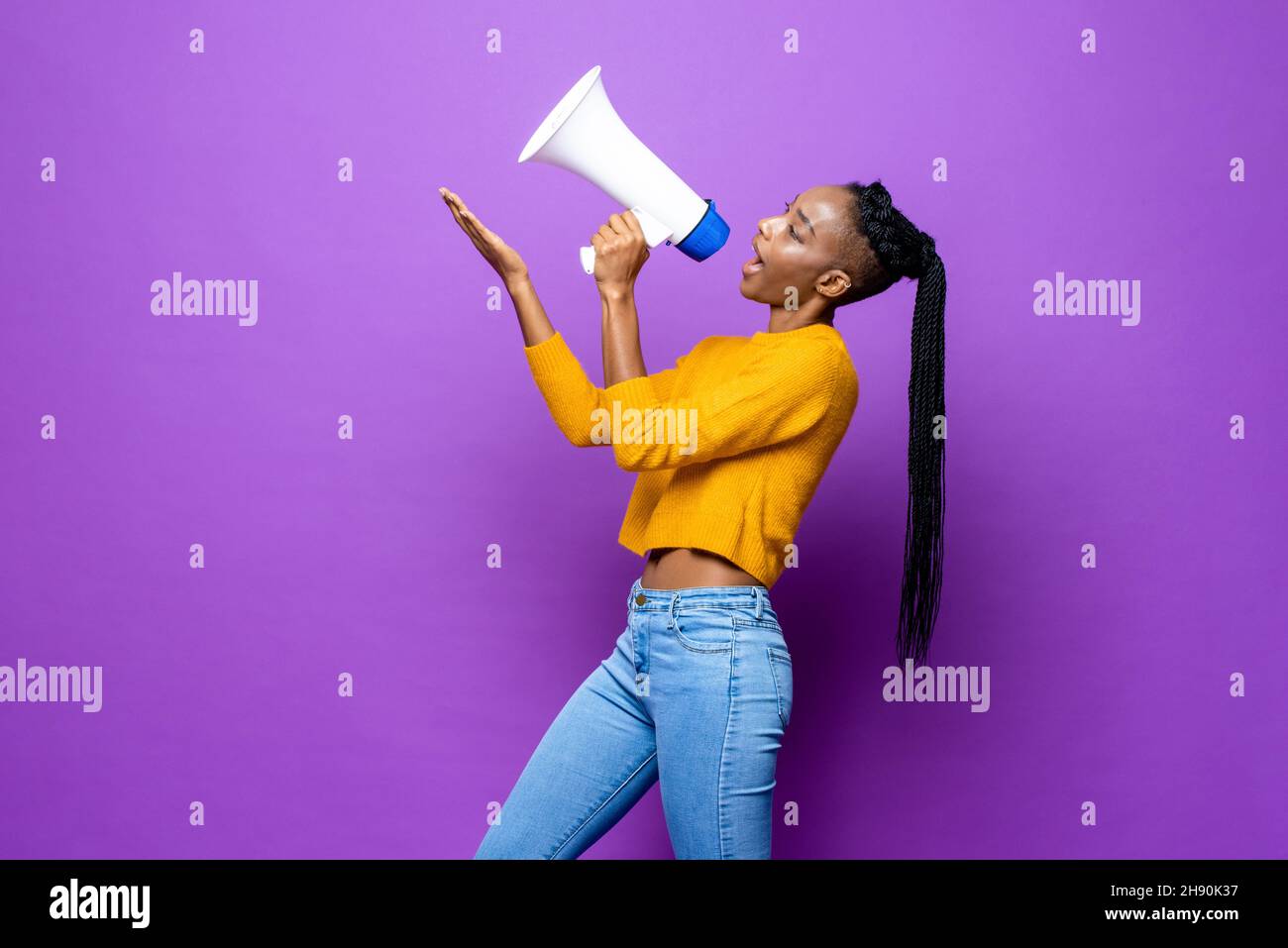 Afroamerikanische Frau, die auf einem Megaphon spricht und mit der Hand nach oben zeigt, auf einem isolierten violetten Hintergrund im Studio Stockfoto