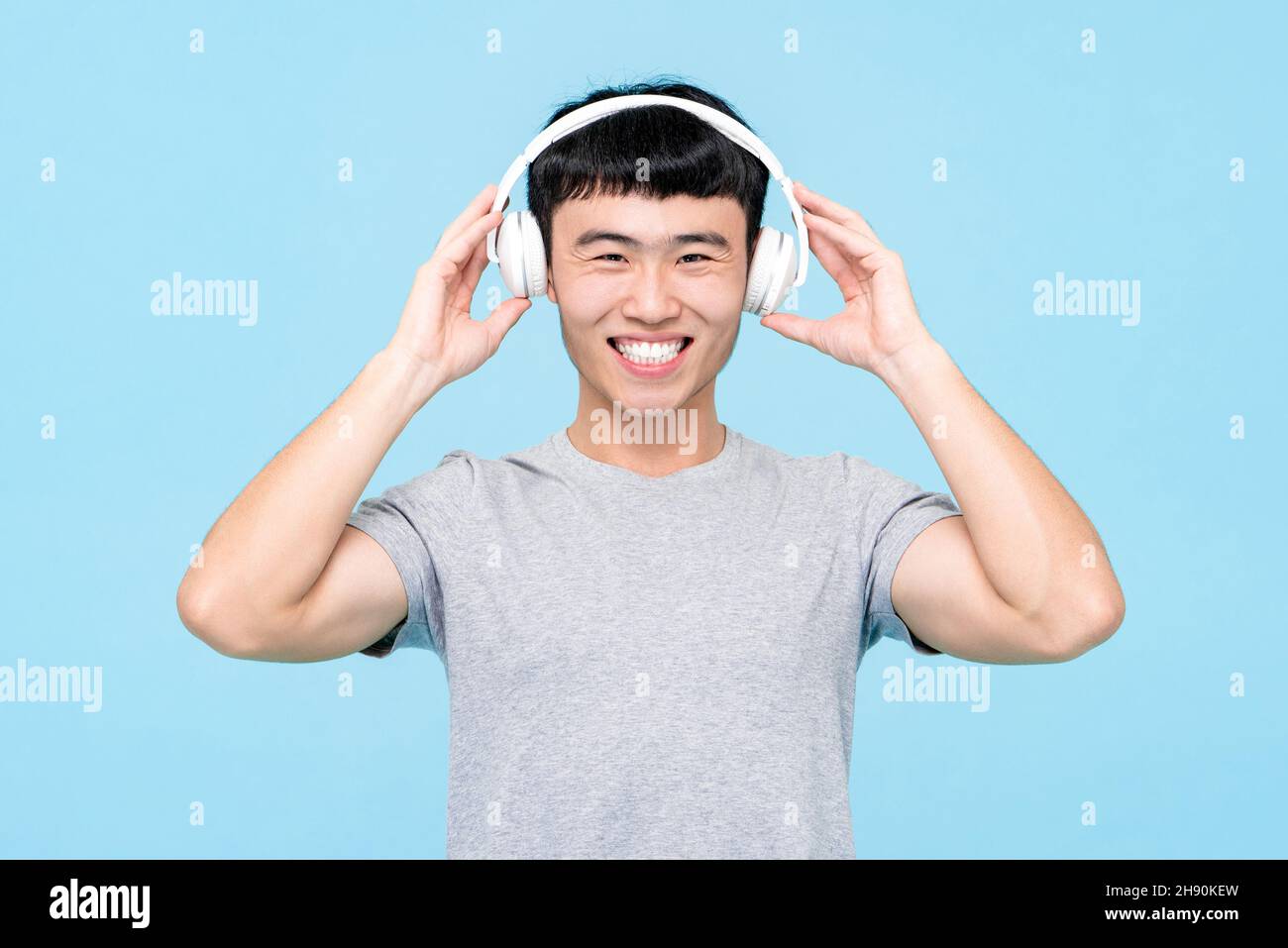 Musikportrait eines jungen, fröhlichen asiatischen Mannes mit einem kabellosen Kopfhörer, der Lieder auf einem isolierten hellblauen Hintergrund hört Stockfoto