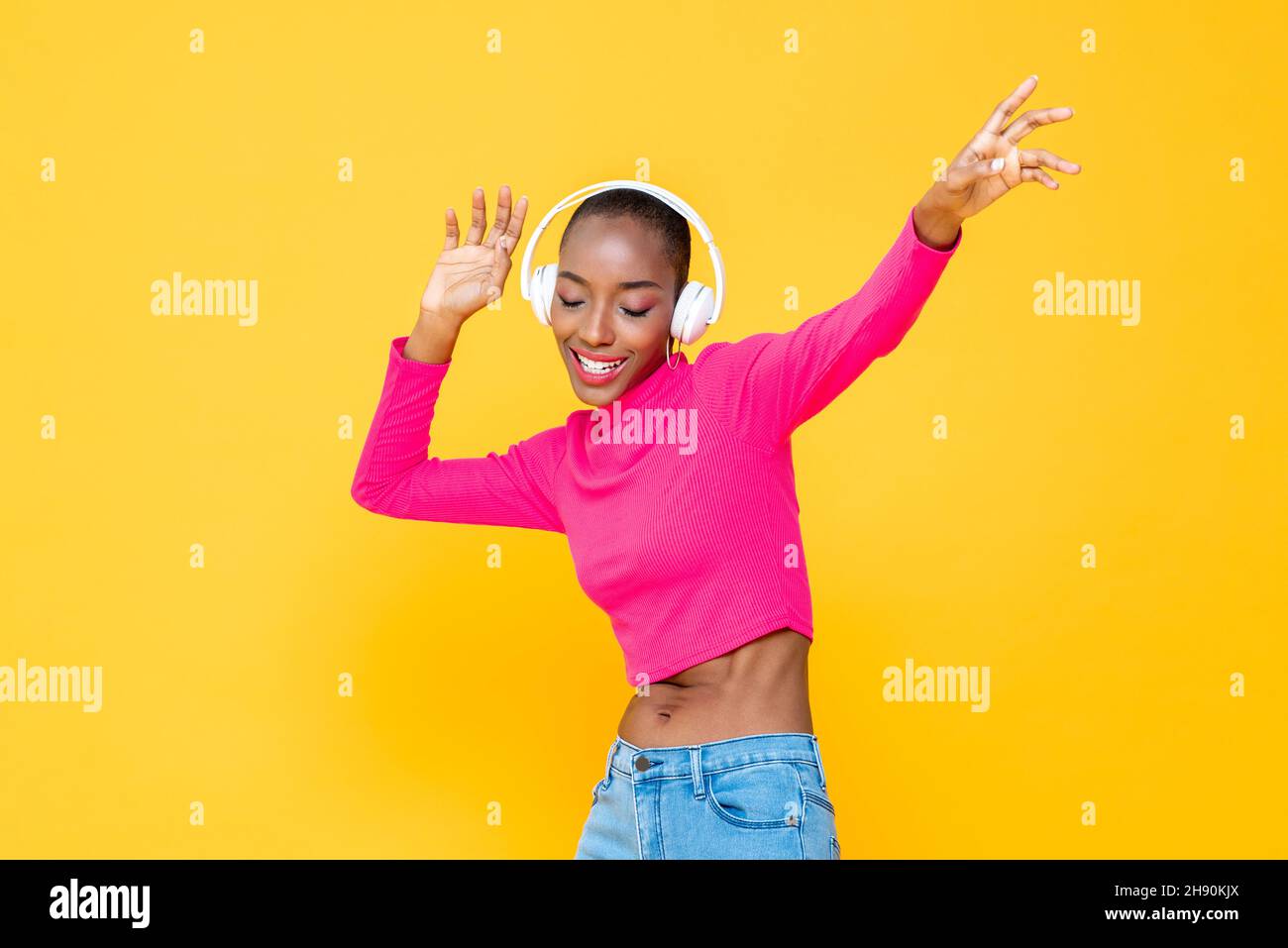 Glückliche afroamerikanische Frau trägt Kopfhörer Musik hören und tanzen auf bunten gelb isolierten Hintergrund Stockfoto