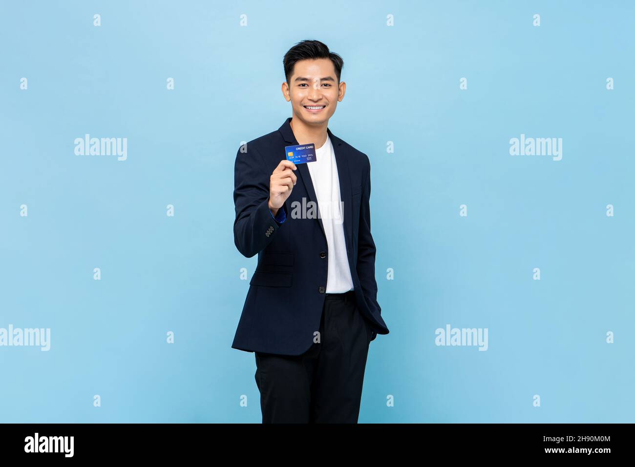 Hübscher südostasiatischer Mann im Stehen und zeigt Kreditkarte in hellblauer Farbe isoliert Studio Hintergrund Stockfoto