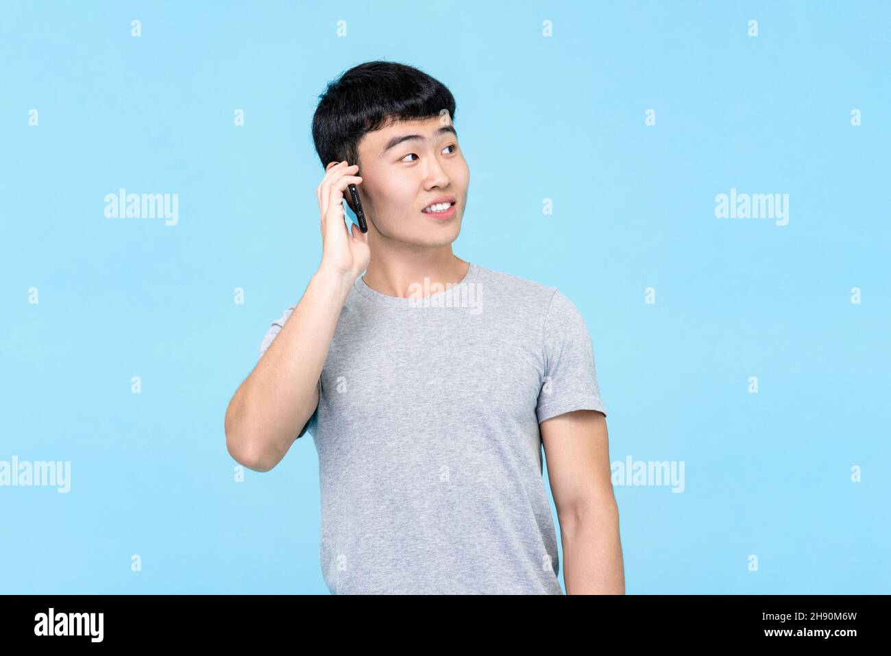 Fröhlicher junger asiatischer Mann, der auf einem Mobiltelefon spricht, isoliert auf blauem Studiohintergrund Stockfoto