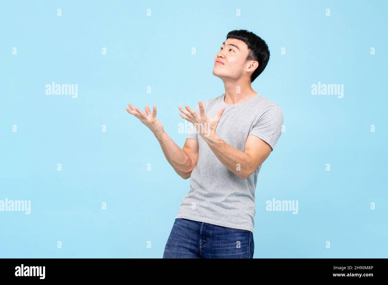 Asiatischer Mann, der mit einem schockierten Gesicht die Hände aufhob und auf einem hellblauen Hintergrund auf leeren Raum über dem Studio schaute Stockfoto