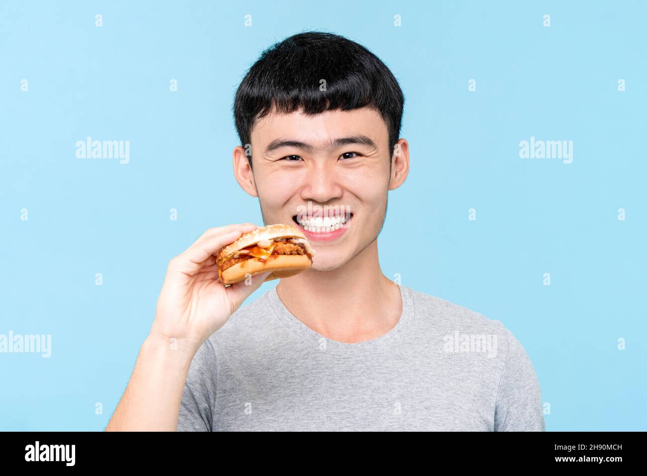 Junger asiatischer Mann sucht Hamburger in hellblau isoliert Hintergrund Stockfoto