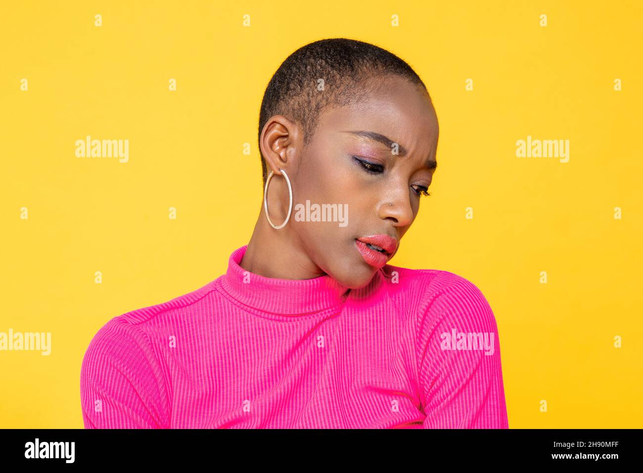 Junge afroamerikanische Frau, die sich traurig fühlt und im gelben, isolierten Studiohintergrund herunterschaut Stockfoto