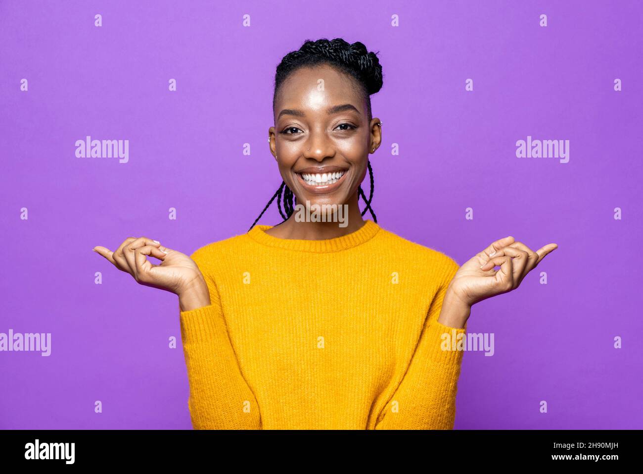 Porträt einer lächelnden jungen afroamerikanischen Frau, die in einem isolierten, violetten Studiohintergrund die Hände zur Seite zeigt Stockfoto
