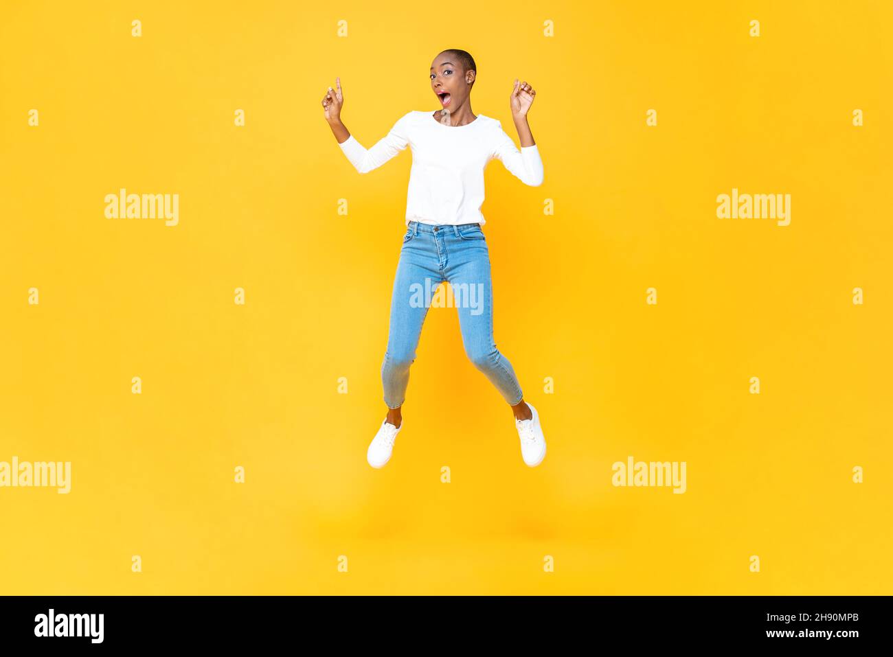 Energische junge afroamerikanische Frau, die mit der Hand nach oben in einem isolierten gelben Studiohintergrund springt Stockfoto