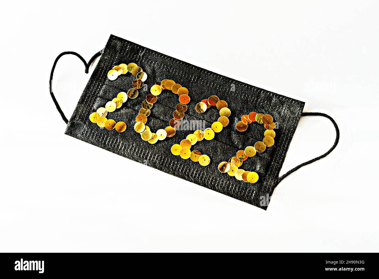 Schwarze medizinische Gesichtsschutzmaske mit Neujahr 2022 Zahlen aus goldenen Pailletten auf weißem Hintergrund Nahaufnahme Stockfoto