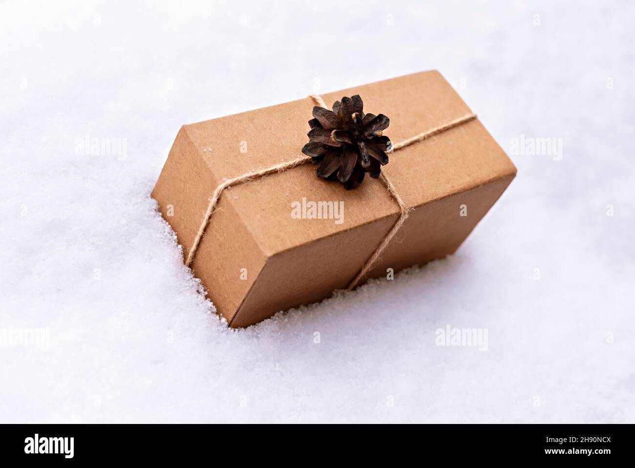 Geschenk in Bastelkiste mit Kieferkegel auf weißem Schnee, umweltfreundliche Öko-Konzept Weihnachten und Neujahr Null Abfall dekoriert Stockfoto