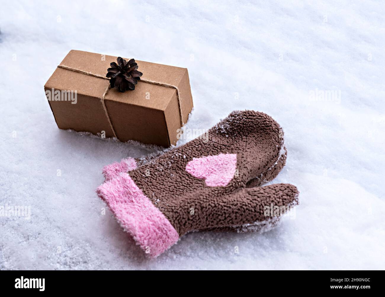 Geschenk in einer Bastelkiste mit Kieferkegel auf weißem Schnee und Fäustlinge mit rosa Herz, umweltfreundliche Öko-Konzept Frohe Weihnachten und Neujahr dekoriert Stockfoto