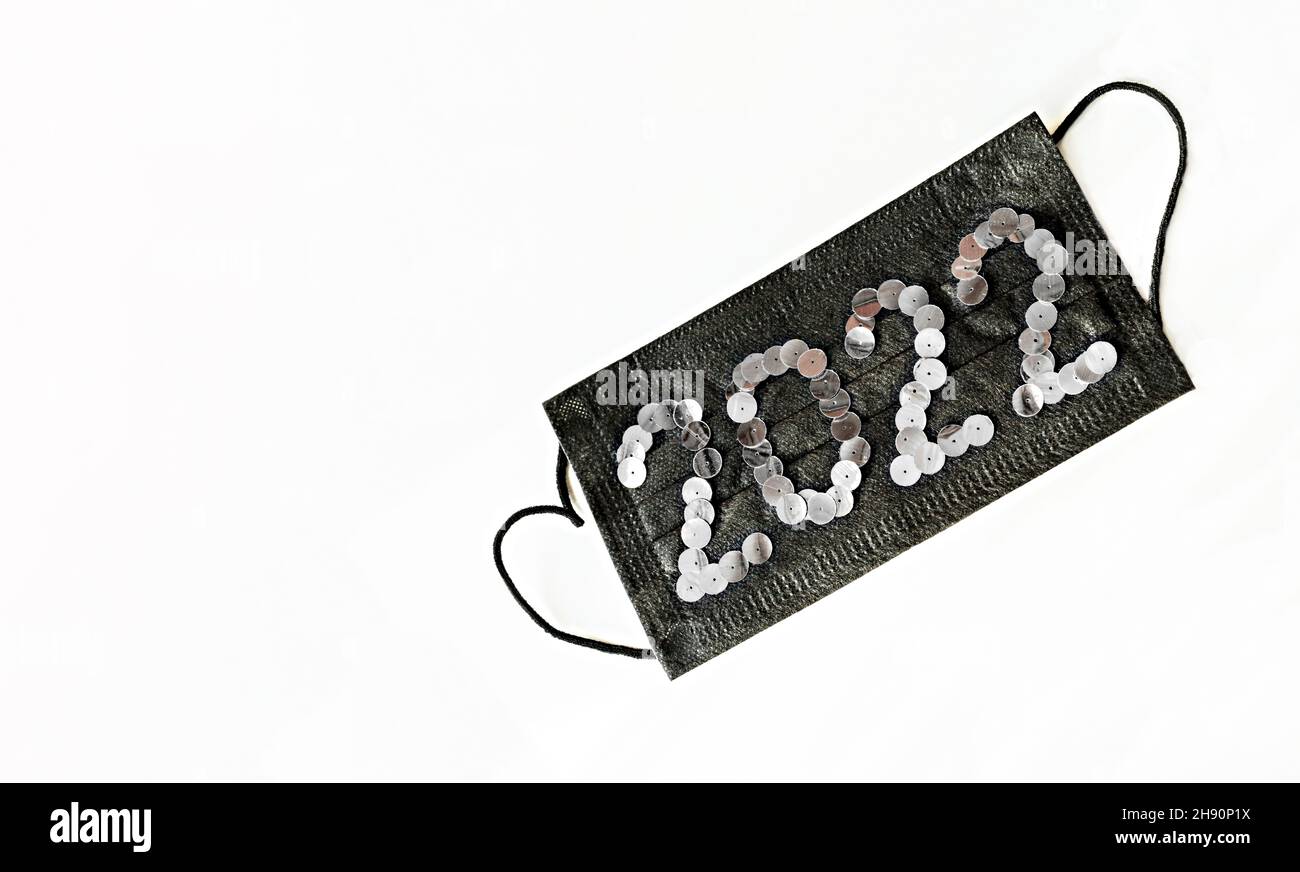 Schwarze medizinische Gesichtsschutzmaske mit Neujahr 2022 Zahlen aus Pailletten auf weißem Hintergrund Nahaufnahme gesunde Neujahr Konzept Kopieplatz Stockfoto