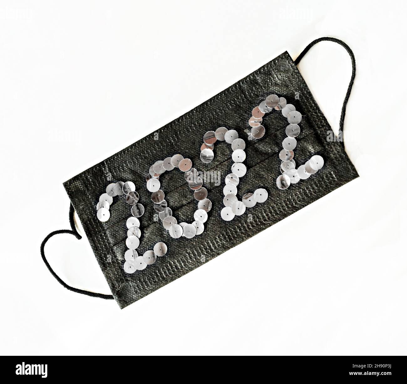 Schwarze medizinische Gesichtsschutzmaske mit Neujahr 2022 Zahlen aus silbernen Pailletten auf weißem Hintergrund Nahaufnahme gesundes Neujahrskonzept Stockfoto