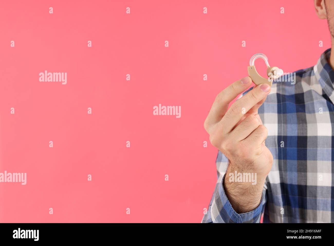 Junger Mann hält Hörgeräte auf rosa Hintergrund Stockfoto