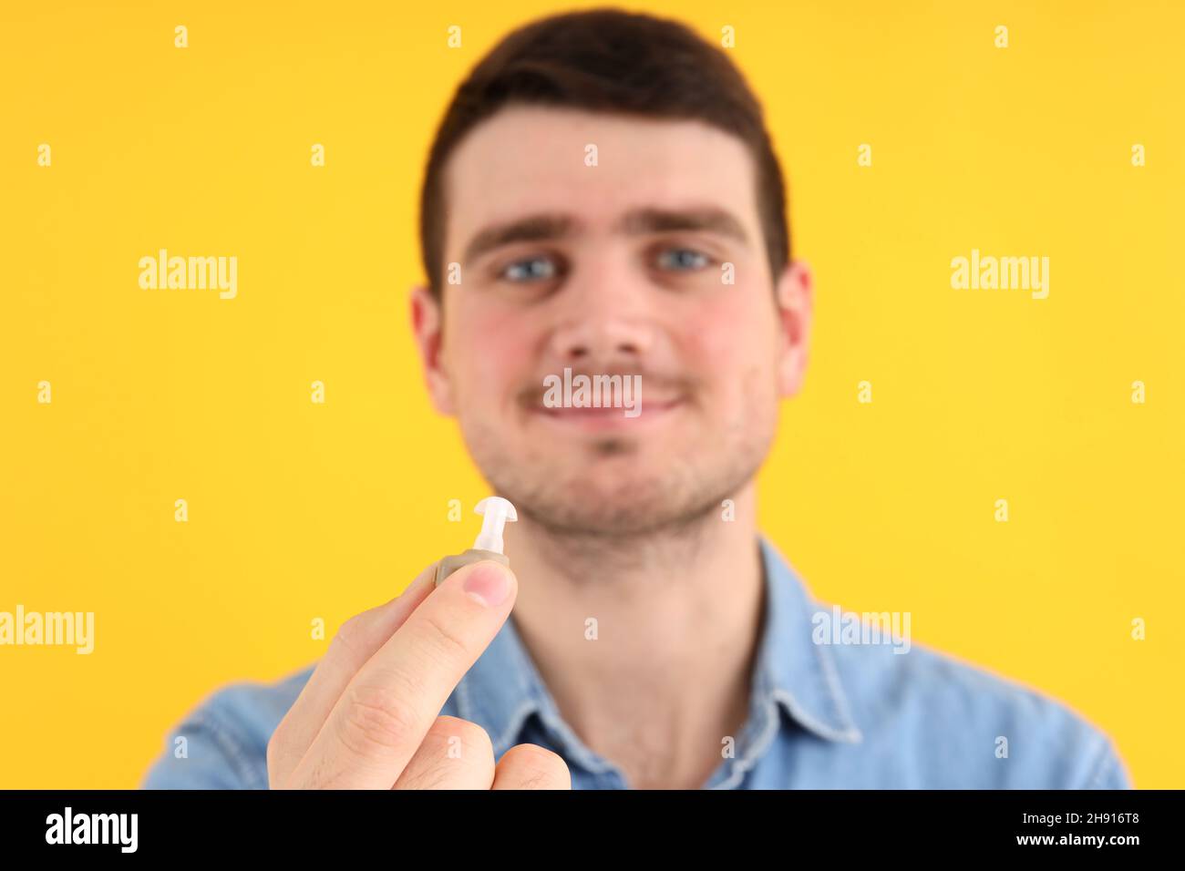 Junger Mann hält Hörgeräte auf gelbem Hintergrund Stockfoto