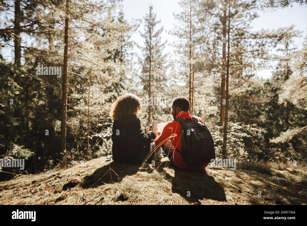 Heterosexuelles Paar, das während des Urlaubs aus einem isolierten Behälter im Wald trinkt Stockfoto